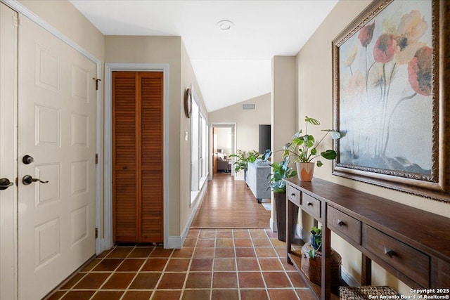 corridor featuring lofted ceiling, dark tile patterned floors, visible vents, and baseboards