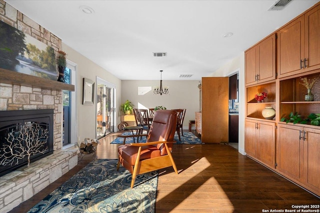 interior space with a chandelier, visible vents, dark wood finished floors, and a stone fireplace