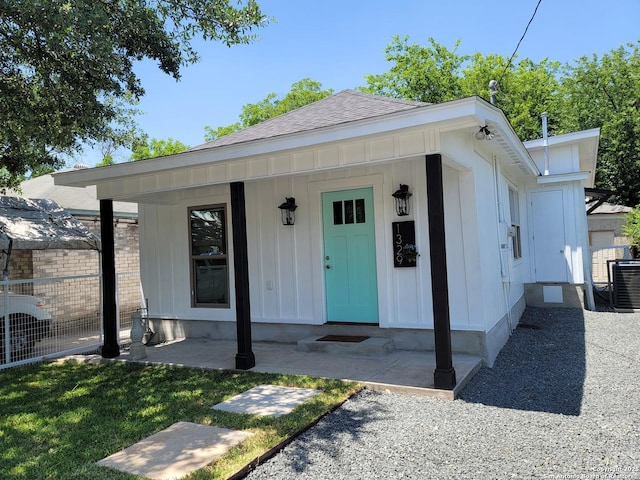 view of front of house with board and batten siding, central AC, a shingled roof, and fence