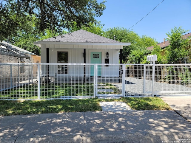 bungalow featuring a fenced front yard, covered porch, roof with shingles, and board and batten siding