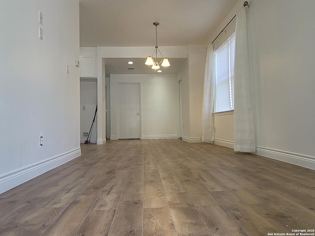 unfurnished dining area with baseboards, wood finished floors, and a notable chandelier