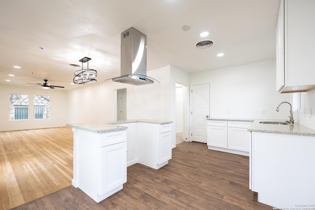 kitchen featuring visible vents, dark wood finished floors, island exhaust hood, white cabinetry, and a sink