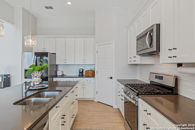 kitchen with a sink, visible vents, white cabinetry, appliances with stainless steel finishes, and dark countertops