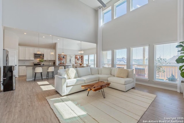 living area featuring light wood-type flooring, baseboards, and a high ceiling