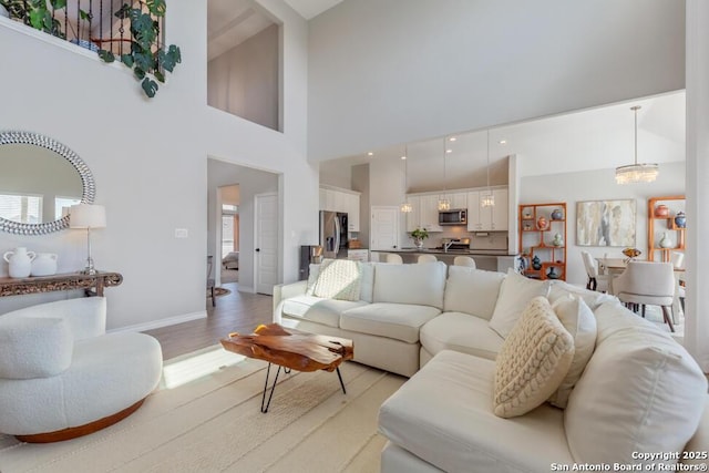 living area featuring a chandelier, baseboards, a towering ceiling, and light wood finished floors