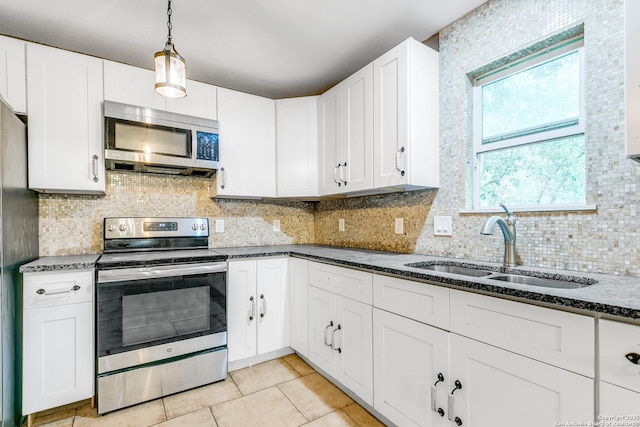 kitchen featuring appliances with stainless steel finishes, a sink, decorative backsplash, and dark stone countertops