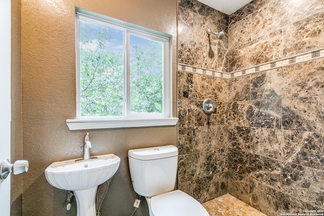 full bath featuring a sink, a textured wall, a tile shower, and toilet