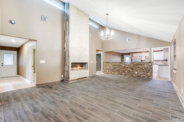 unfurnished living room with a chandelier, wood tiled floor, a large fireplace, and visible vents