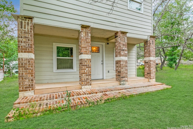 entrance to property with covered porch, brick siding, and a lawn