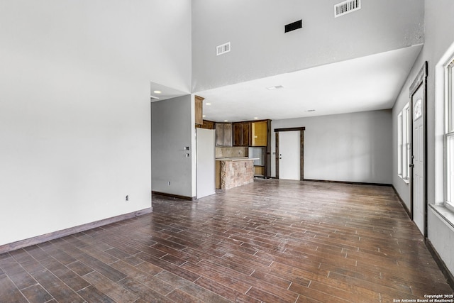 unfurnished living room featuring a towering ceiling, baseboards, visible vents, and dark wood finished floors