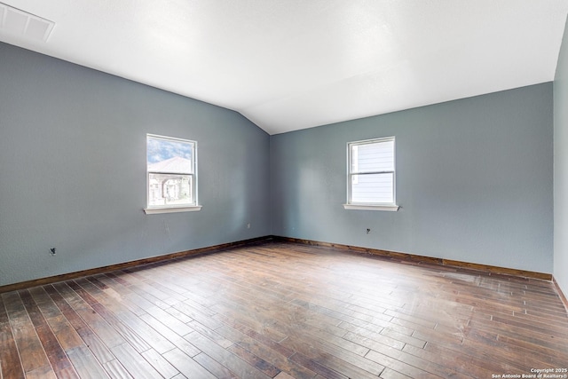 spare room featuring lofted ceiling, a healthy amount of sunlight, visible vents, and wood finished floors