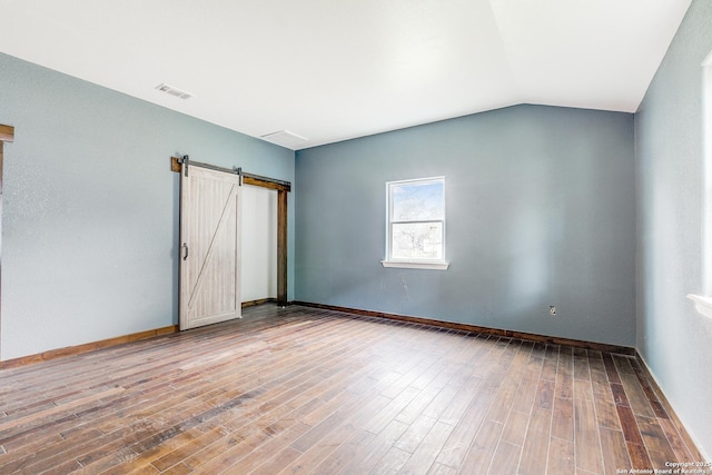 unfurnished room featuring lofted ceiling, a barn door, wood finished floors, visible vents, and baseboards