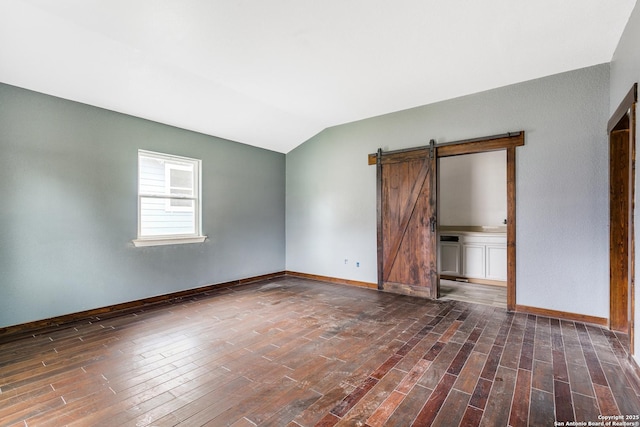 empty room with a barn door, baseboards, vaulted ceiling, and wood finished floors