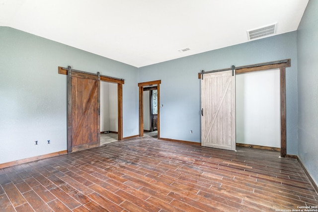 unfurnished bedroom featuring baseboards, a barn door, visible vents, and wood finished floors