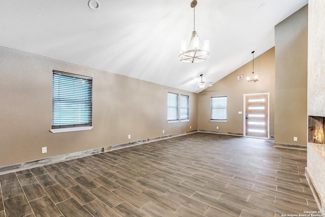 unfurnished living room with high vaulted ceiling, baseboards, ceiling fan with notable chandelier, and wood finish floors