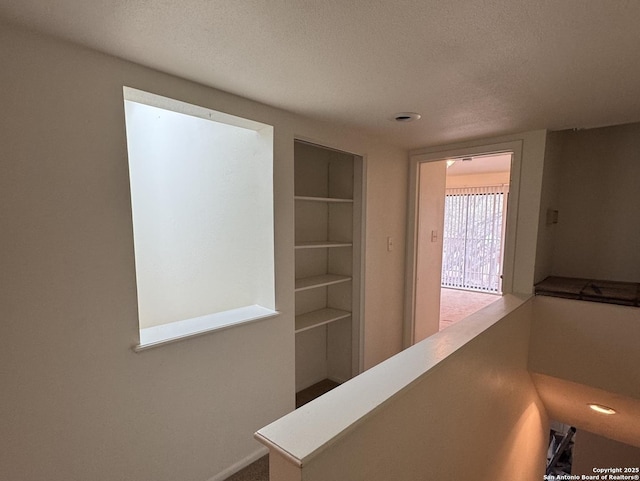 corridor with built in shelves, a textured ceiling, and an upstairs landing