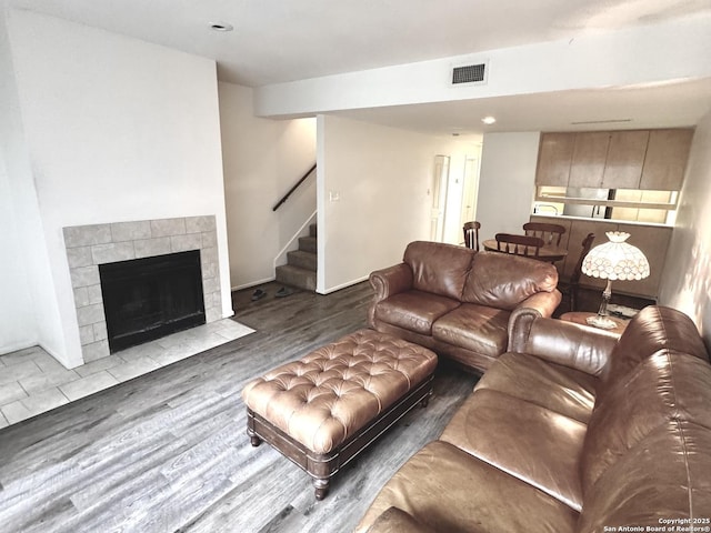 living area with visible vents, stairway, a tiled fireplace, and wood finished floors