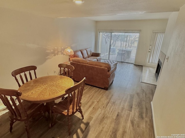 dining area featuring a textured ceiling, a fireplace, light wood-style flooring, and baseboards