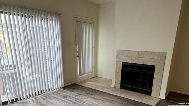 interior space with wood finished floors, a tile fireplace, and baseboards