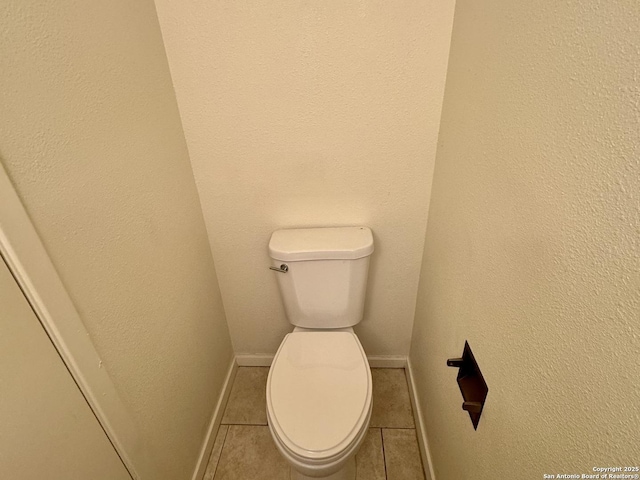 bathroom featuring a textured wall, tile patterned flooring, toilet, and baseboards