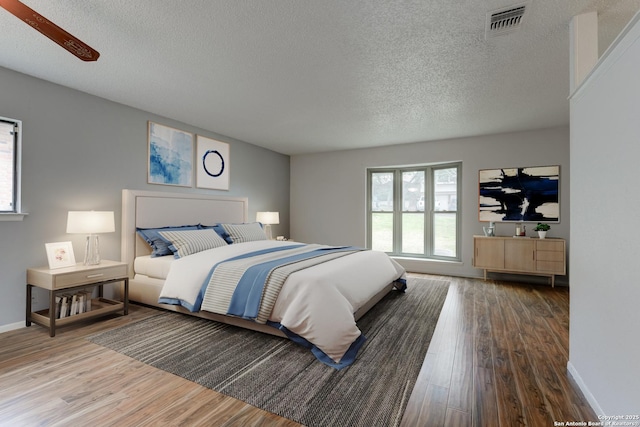 bedroom featuring a textured ceiling, wood finished floors, visible vents, and baseboards