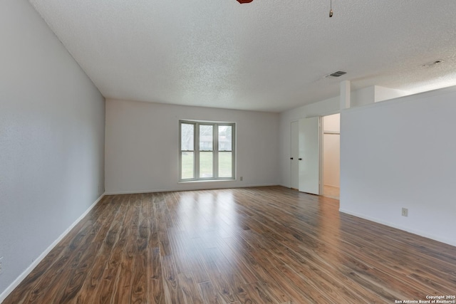 empty room with a textured ceiling, wood finished floors, visible vents, and baseboards