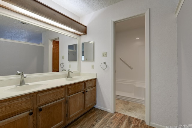 full bathroom featuring a textured ceiling, double vanity, wood finished floors, and a sink