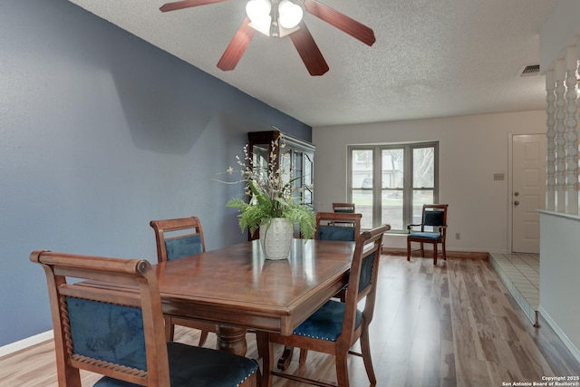 dining room with a textured ceiling, light wood-style flooring, visible vents, a ceiling fan, and baseboards