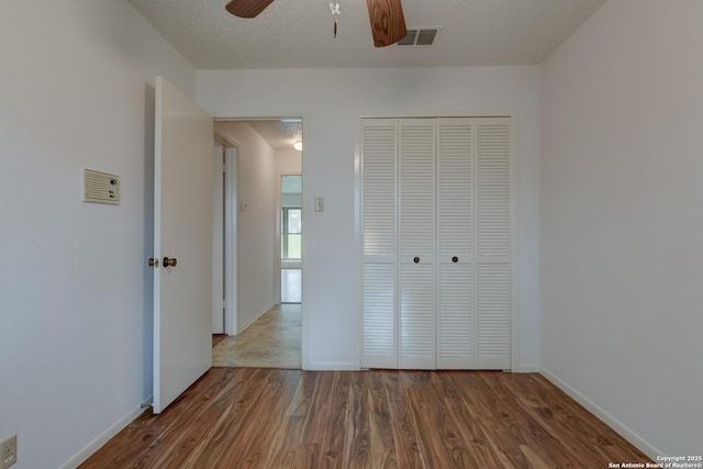 unfurnished bedroom featuring a closet, visible vents, a textured ceiling, wood finished floors, and baseboards