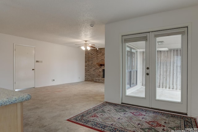 interior space with a ceiling fan, a textured ceiling, french doors, carpet floors, and a fireplace