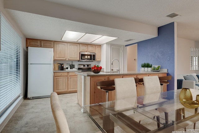 kitchen with a textured ceiling, light brown cabinets, stainless steel appliances, a sink, and visible vents