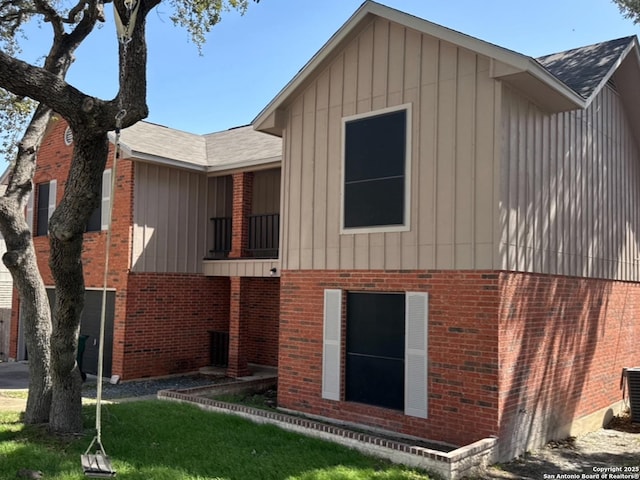 rear view of property with board and batten siding, a lawn, and brick siding