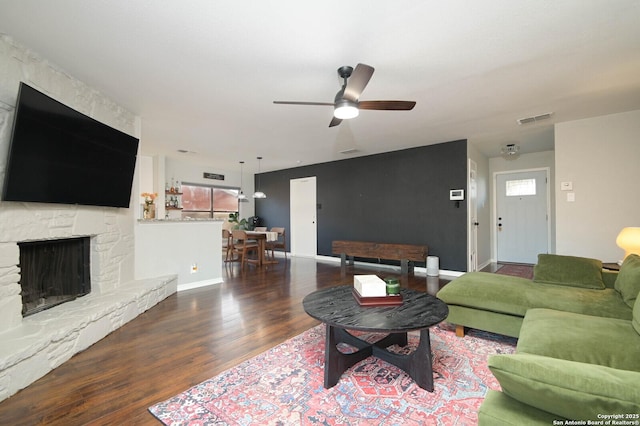 living area with visible vents, a stone fireplace, baseboards, and wood finished floors