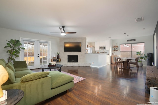 living room with dark wood-style floors, a stone fireplace, a wealth of natural light, and french doors