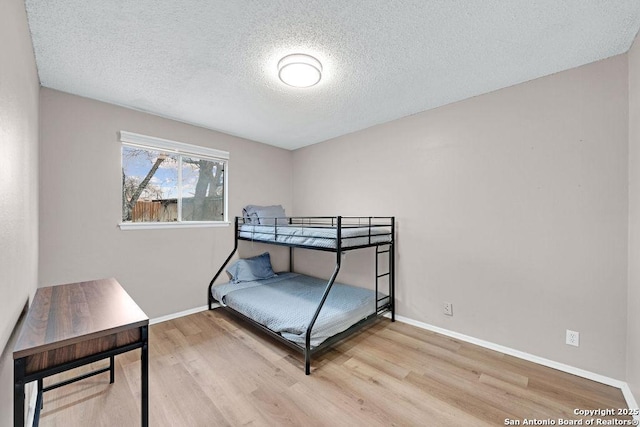 bedroom with a textured ceiling, wood finished floors, and baseboards