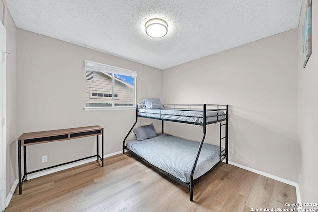 bedroom featuring a textured ceiling, baseboards, and wood finished floors