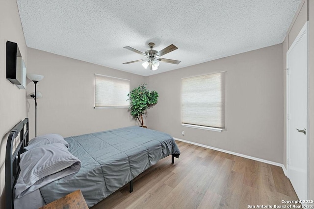 bedroom with a ceiling fan, a textured ceiling, baseboards, and wood finished floors