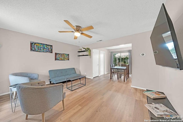 sitting room with a textured ceiling, light wood-type flooring, visible vents, and a ceiling fan