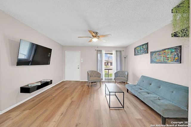 living area featuring a textured ceiling, wood finished floors, a ceiling fan, and baseboards