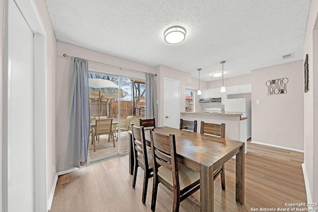 dining space with light wood-style floors, visible vents, a textured ceiling, and baseboards