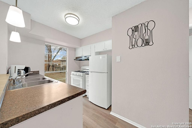 kitchen with white appliances, light wood-style floors, dark countertops, under cabinet range hood, and a sink