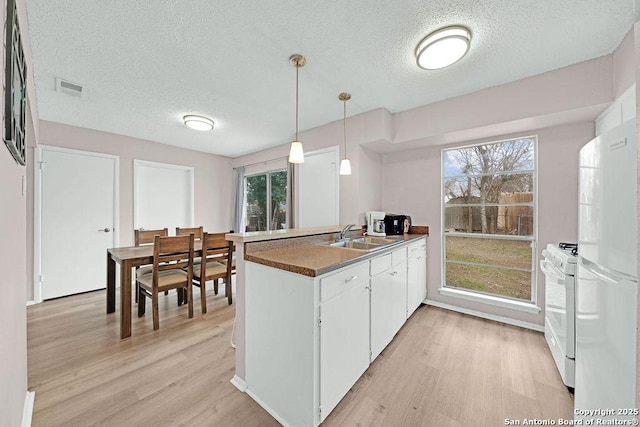 kitchen with a peninsula, white appliances, a sink, visible vents, and dark countertops