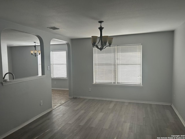 unfurnished dining area featuring wood finished floors, visible vents, baseboards, and an inviting chandelier