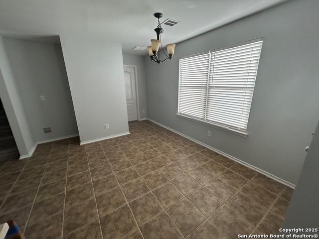 empty room with dark tile patterned floors, baseboards, visible vents, and a notable chandelier