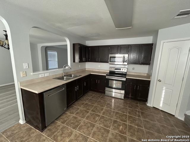 kitchen featuring visible vents, appliances with stainless steel finishes, light countertops, dark tile patterned floors, and a sink