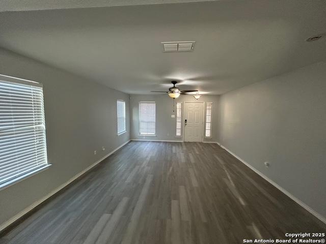 unfurnished living room featuring ceiling fan, dark wood finished floors, visible vents, and baseboards