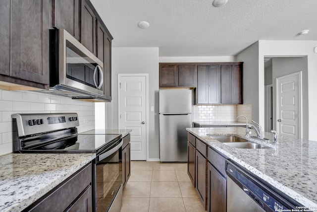 kitchen featuring light tile patterned floors, dark brown cabinetry, stainless steel appliances, a sink, and light stone countertops