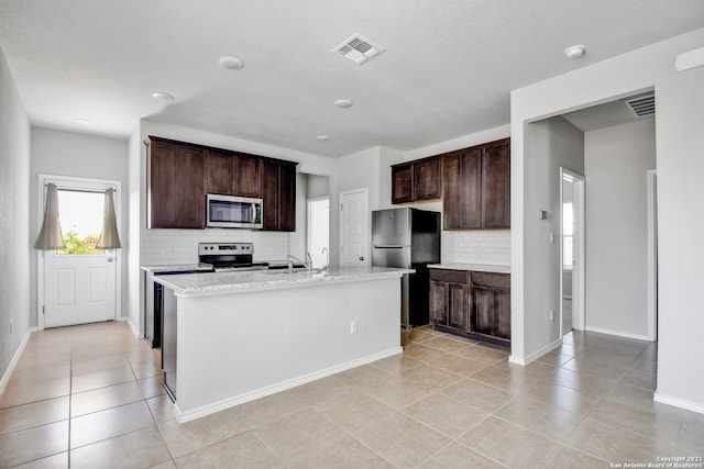 kitchen with dark brown cabinetry, a center island with sink, visible vents, and stainless steel appliances