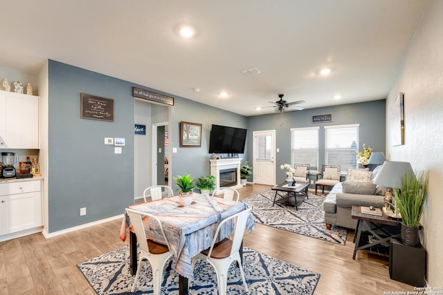 dining room with baseboards, a ceiling fan, a glass covered fireplace, light wood-style flooring, and recessed lighting