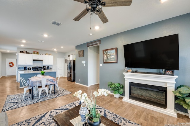 living area featuring ceiling fan, visible vents, baseboards, light wood-style floors, and a glass covered fireplace